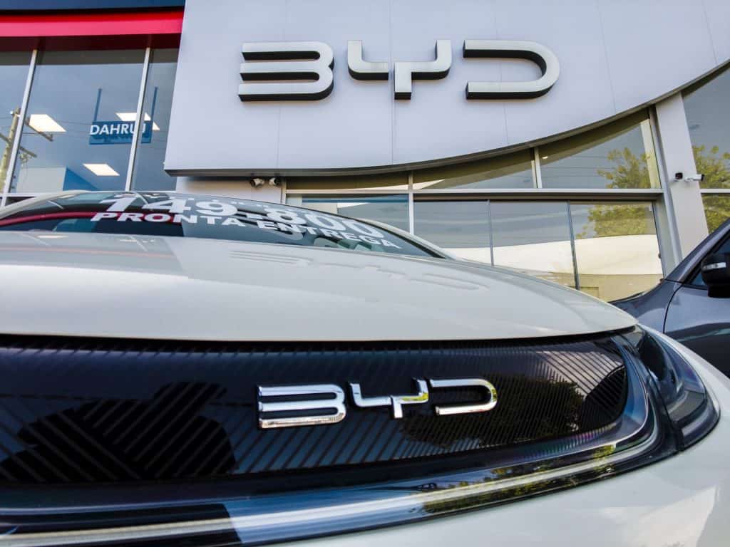 Logo da BYD na fachada de uma loja e na grade de um carro